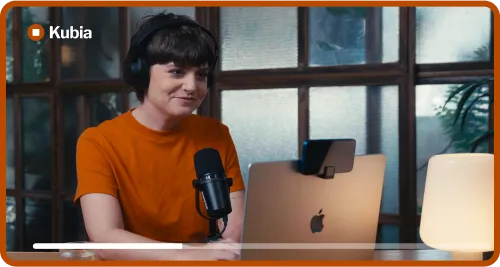 Person with short hair and headphones speaking while using a laptop with a phone mounted on top.